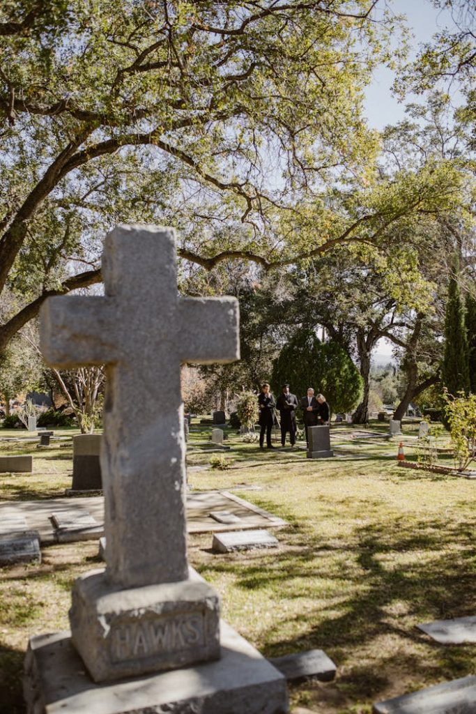 A serene cemetery with a prominent stone cross surrounded by lush greenery and gravestones.